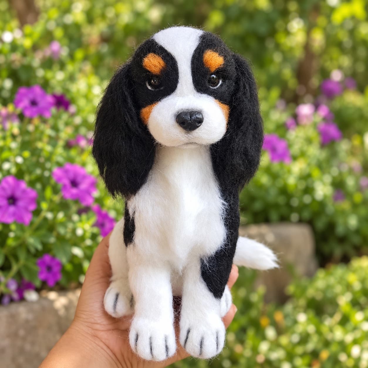 Tricolor Cavalier King Charles Spaniel (CKCS) needle felted dog portrait, front view, sitting in the hand outdoors
